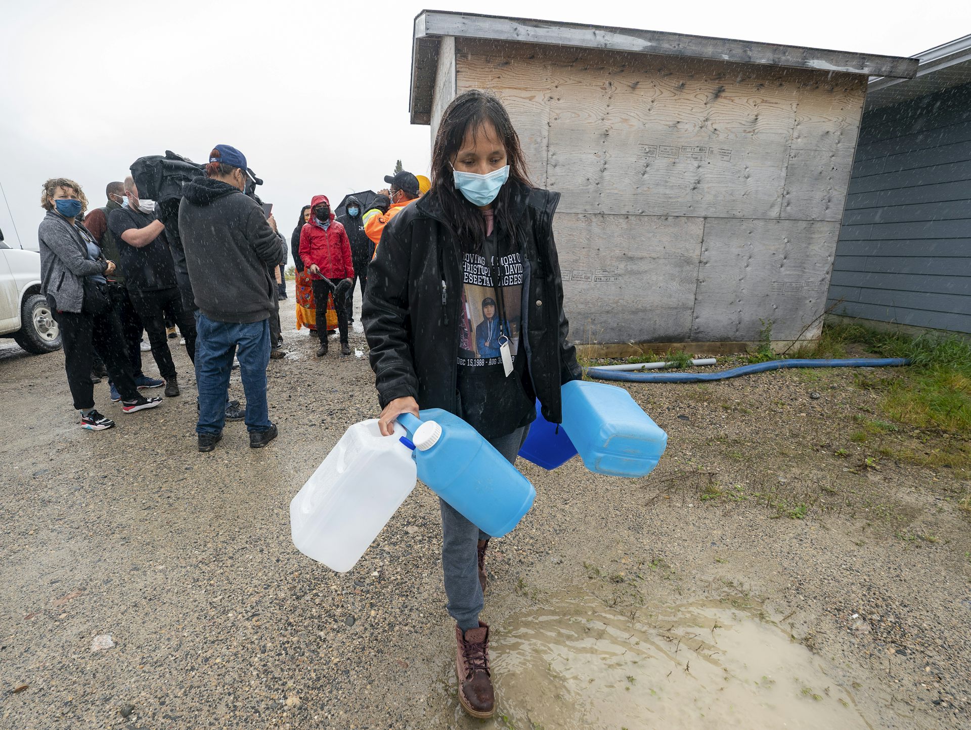A woman carries empty water jugs.