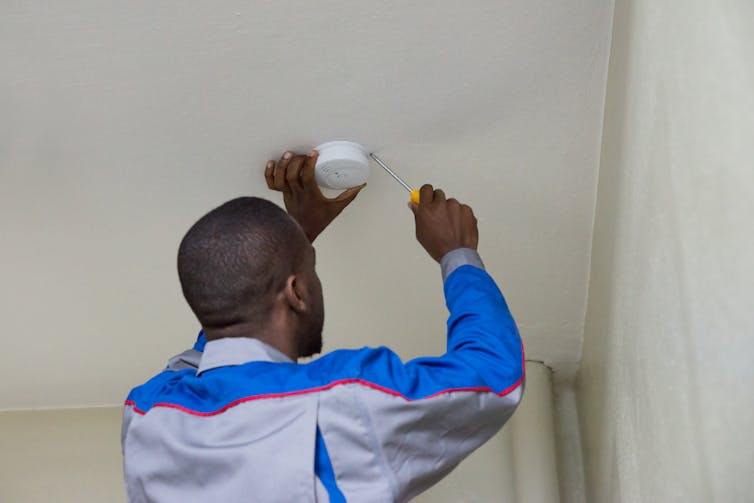 A Black man installs a smoke detector.