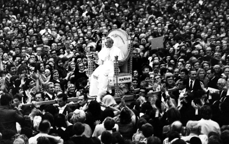 Pope John Paul I, dressed in white, rides on a platform through a crowd.
