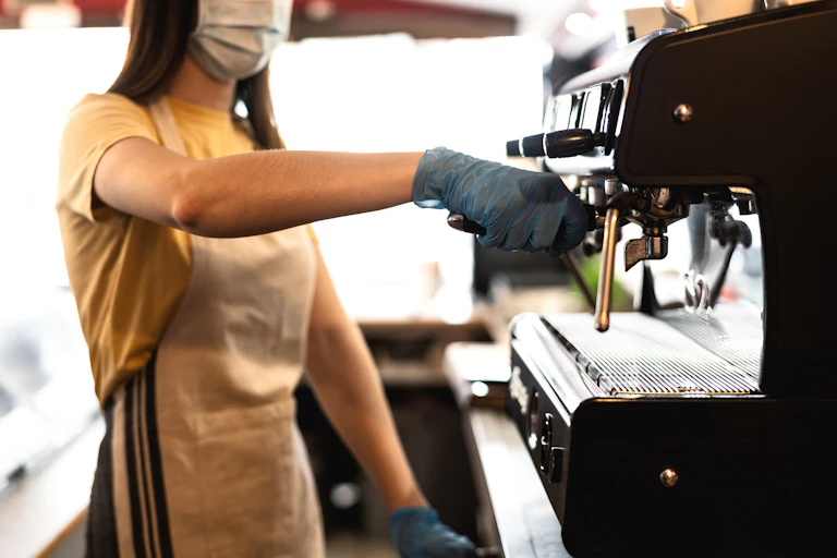 Woman making coffee while wearing mask and gloves