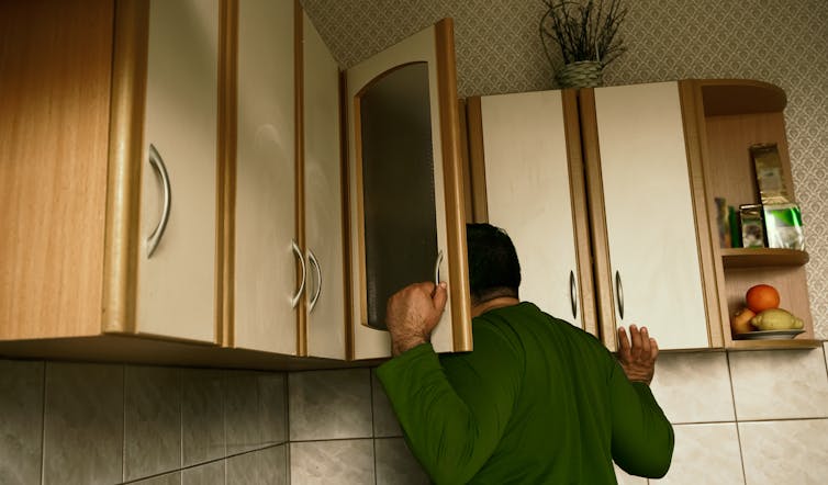 A man looks in his kitchen cupboards.