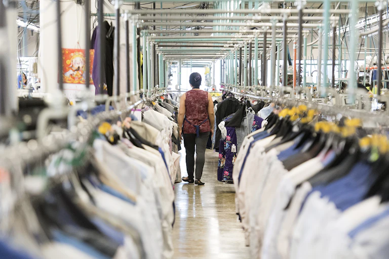 A woman seen from behind walking between two rows of hanging clothing