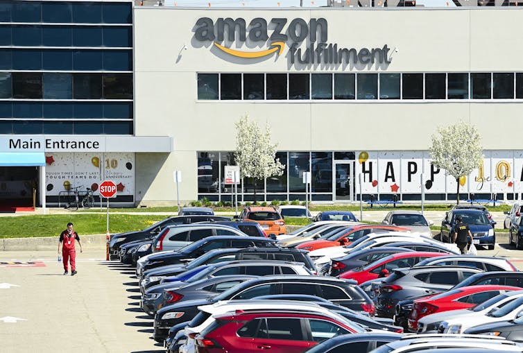 A man walks through a full parking lot outside an Amazon warehouse