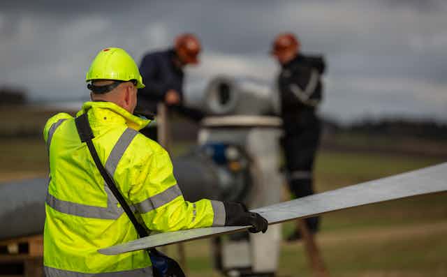 A worker in high-visibility clothing holds a wind turbine blade.