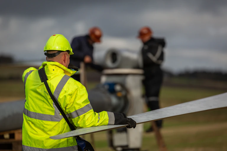 A worker in high-visibility clothing holds a wind turbine blade.