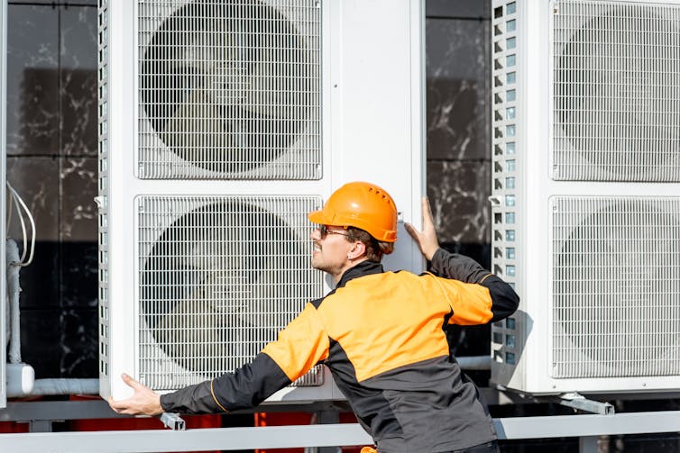 An engineer adjusts the large fan unit of an air-source heat pump.