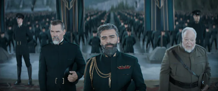 Three men in military uniforms stands before an army.