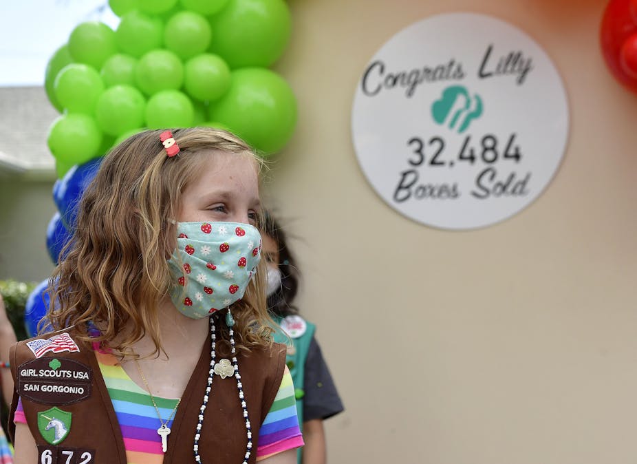 A Girl Scout wearing a mask and her uniform's vest celebrates her sale of 32,484 boxes of cookies.