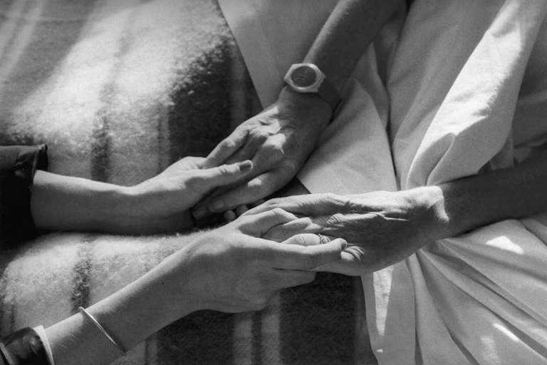 A pair of hands holding the fingers of another on a hospital bed