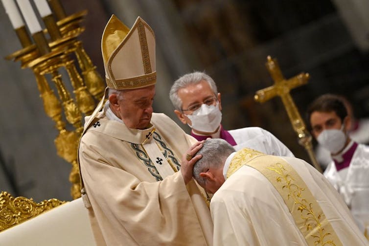 Pope Francis putting his hand on the head of a priest bowing before him.