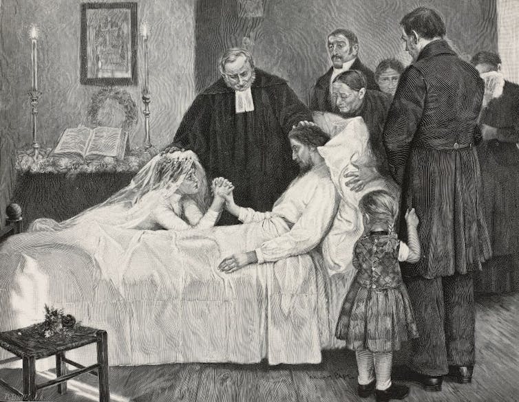 A bride holding the hand of a dying man on his bed with family members surrounding them.