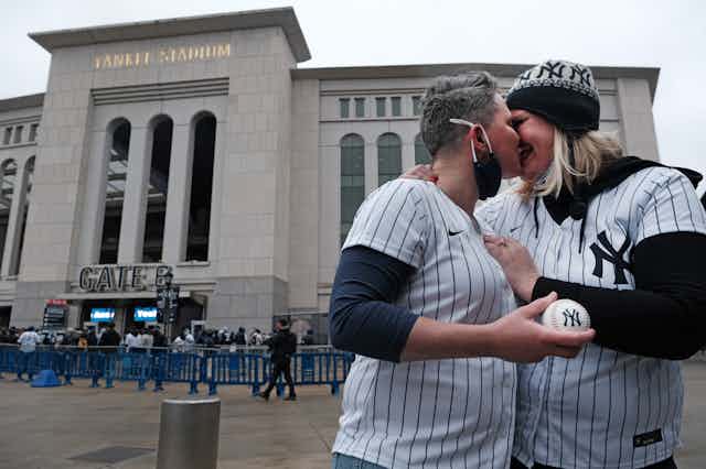 Two women in Yankees jerseys kiss.