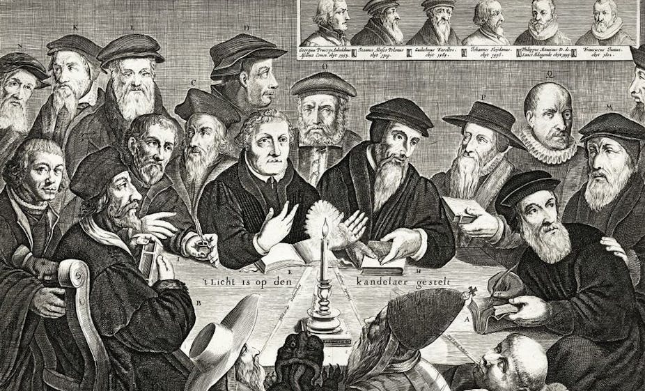 A dozen and a half men, most of them wearing hats, gather around a table with a candle lit on it, in a black and white engraving.