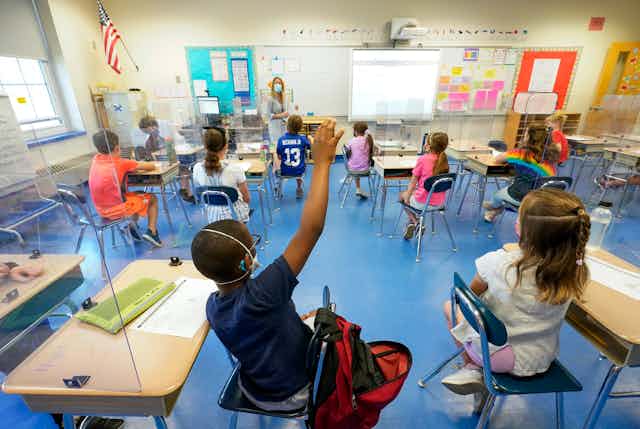 Elementary school kids sit at socially distanced desks in school classroom