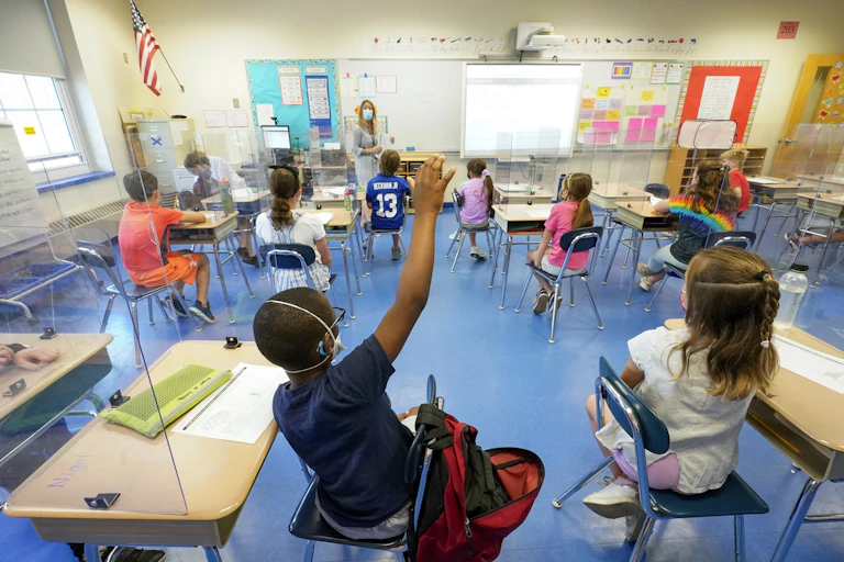 Elementary school kids sit at socially distanced desks in school classroom