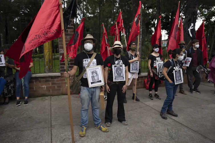 People stand with red flags holding photos of loved ones.