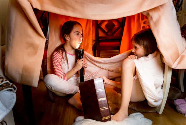 Two girls sitting in a blanket den telling scary stories, one girl scared