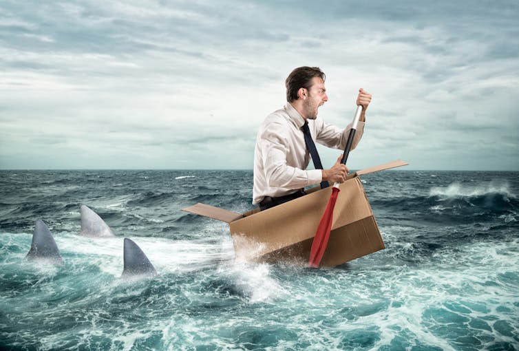 Scared man rowing away from sharks