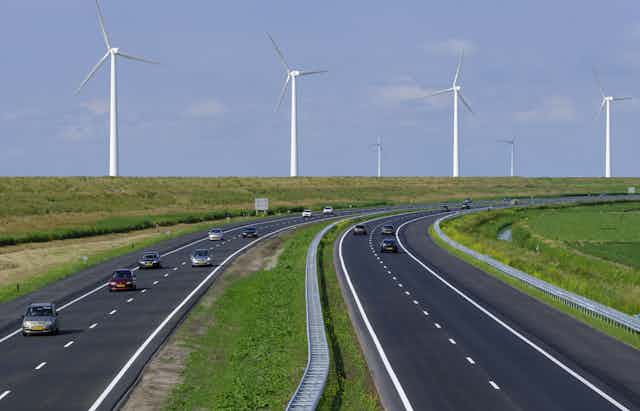 Cars travelling along a motorway, with wind turbines in the background 