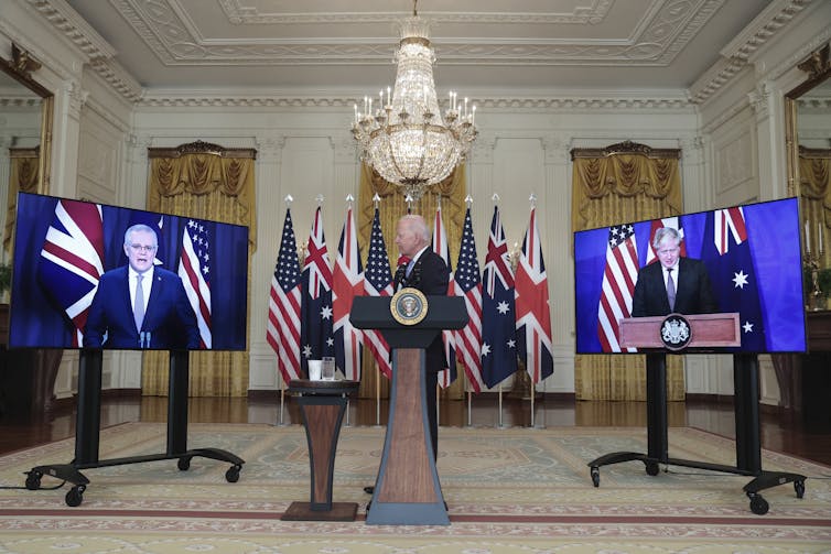 man between two TV screens displaying men's faces