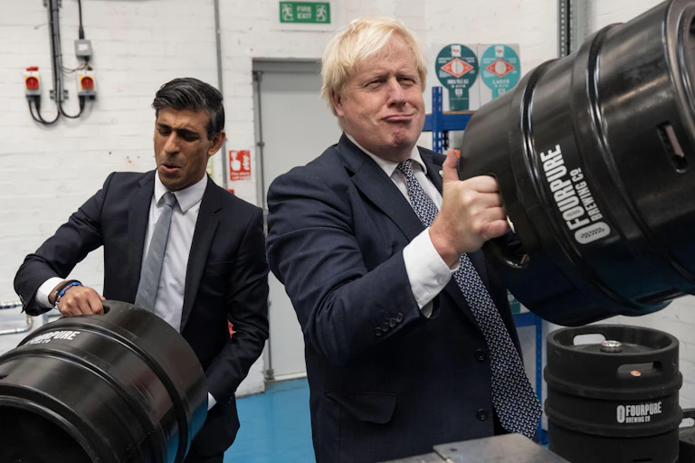 Rishi Sunak and Boris Johnson make faces as the pretend to lift heavy barrels of beer at a brewery.