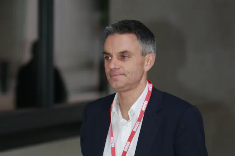 BBC director-general Tim Davie in a suit and open-necked shirt with a BBC lanyard around his neck.