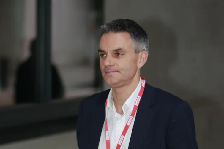 BBC director-general Tim Davie in a suit and open-necked shirt with a BBC lanyard around his neck.