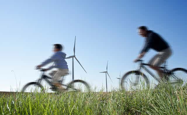 A man and child cycle past wind turbines.