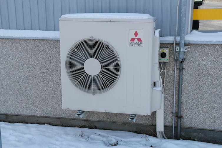 A fan in a large, white box attached to the exterior of a house.
