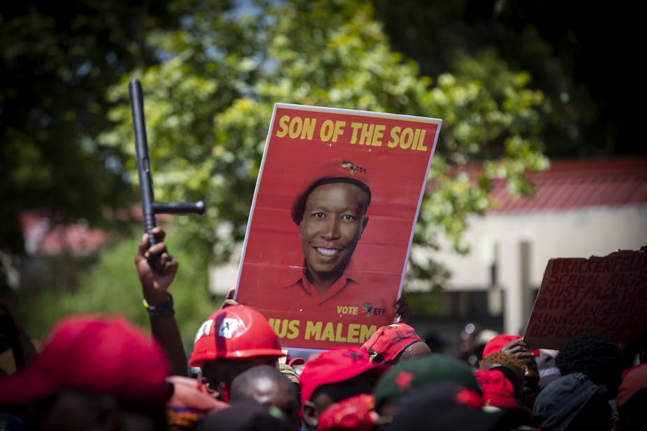 A person in a crowd lifts an election poster featuring the face of Julius Malema, leader of the Economic Freddom Fighters