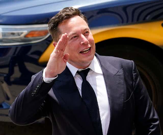 Elon Musk salutes as he stands in front of a car