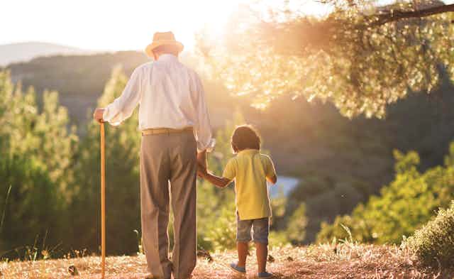 Older man holds child's hand and walks with a cane