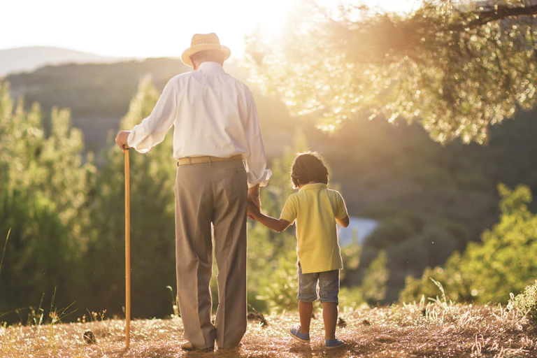 Older man holds child's hand and walks with a cane