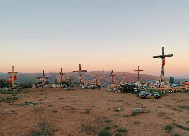 A handful of wooden crosses decorated with personal mementos stand on a hilltop.