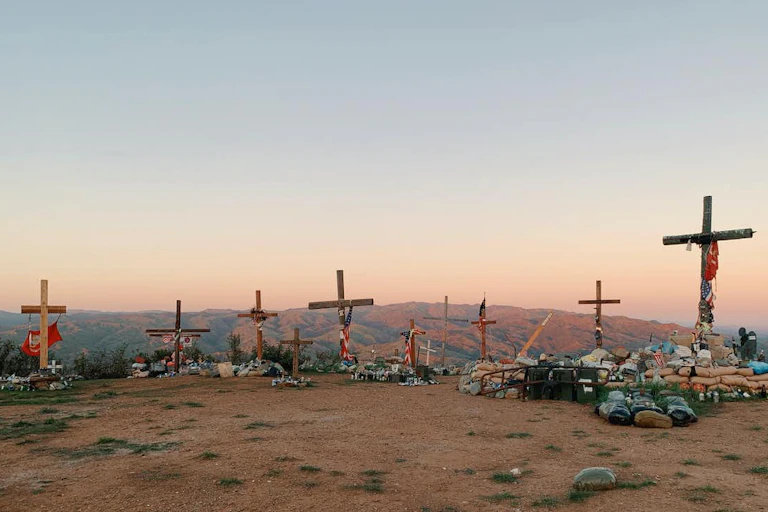 A handful of wooden crosses decorated with personal mementos stand on a hilltop.