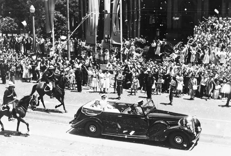The Queen in a car driving past a crowd.