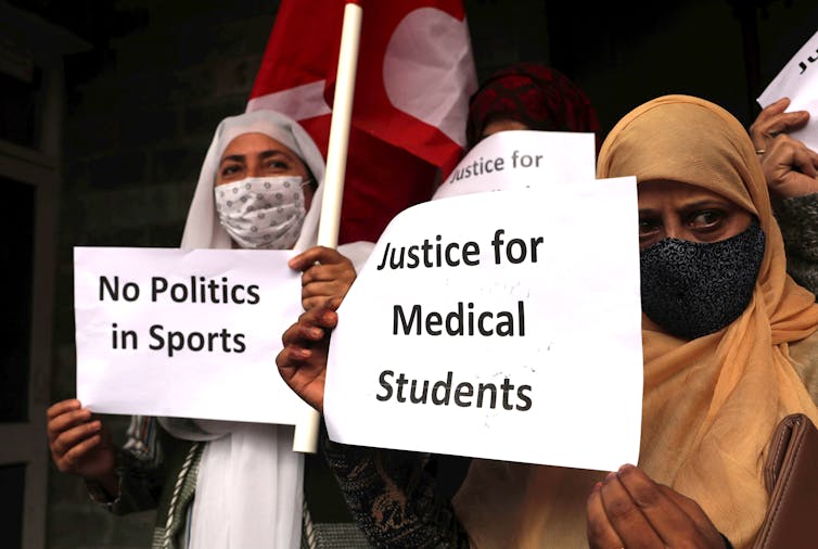 Women wearing COVID masks hold up placards in English condemning the arrest of media students for celebrating Pakistan's win in a ercent cricket match.
