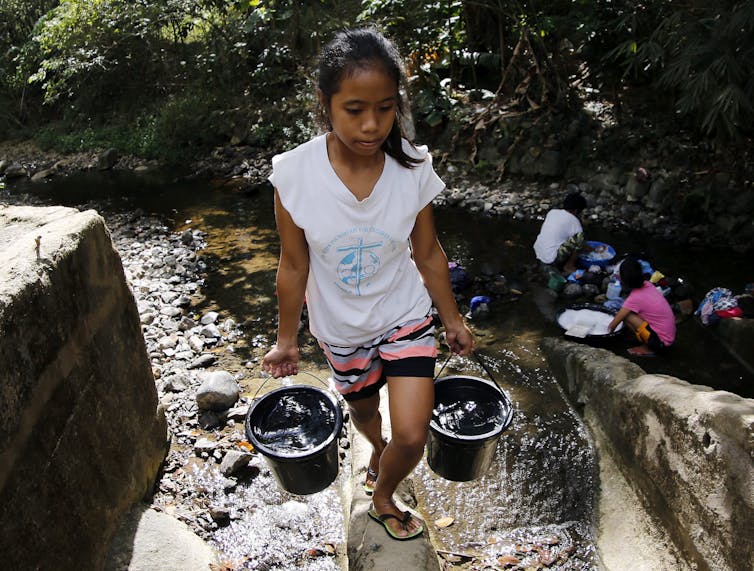 girl carries buckets of water from stream