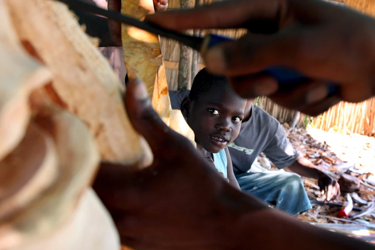 boy looks through hands carving wood