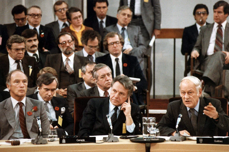 Three men in suits sit at a long desk with microphones in front of them.