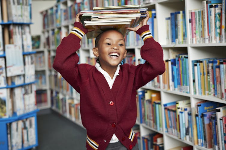 Smiling girl in school uniform holds stack of books on her head