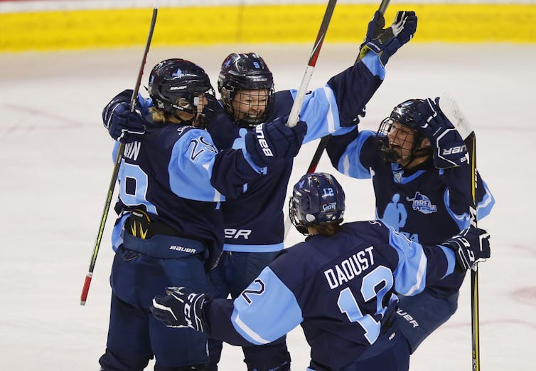 Women hockey players wearing blue uniforms jump up in celebration