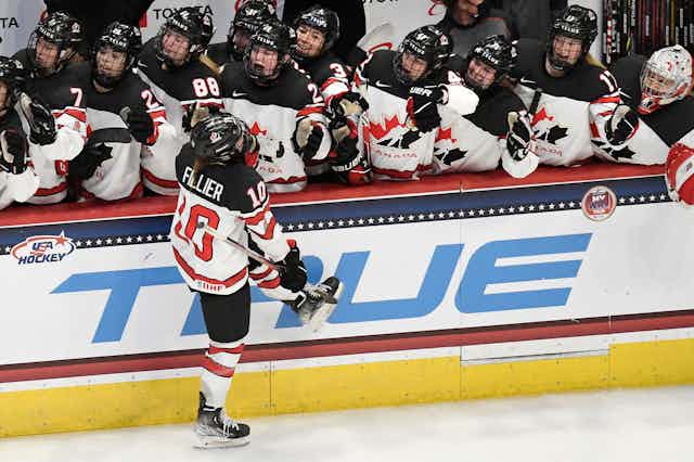 A woman wearing a team Canada jersey skates past and highfives her teammates