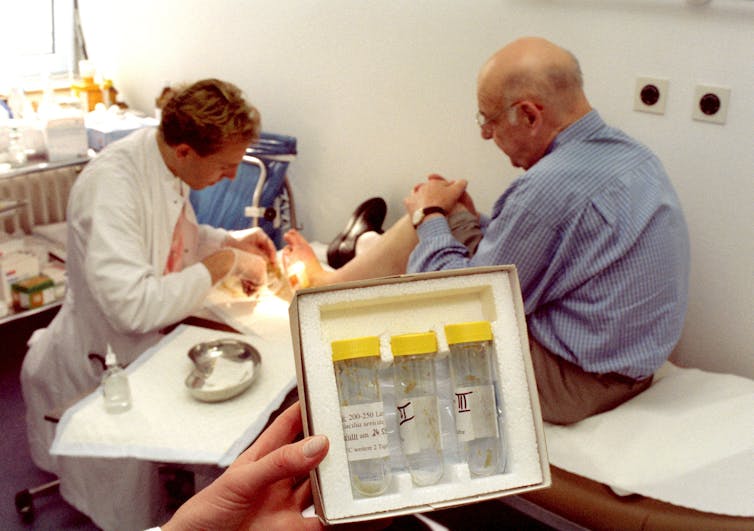 doctor working on patient's foot in background, tubes of maggots in foreground