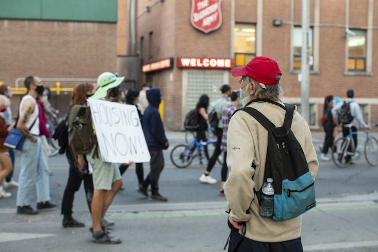 A man, standing outside a Salvation Army drop-in centre for the homeless, watches as protesters calling for empty buildings to be used for housing for the homeless pass by,