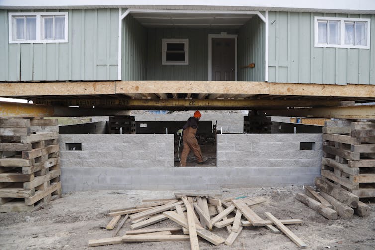 Una casa levantada sobre pilares con una nueva base de bloques de hormigón que se está construyendo debajo.