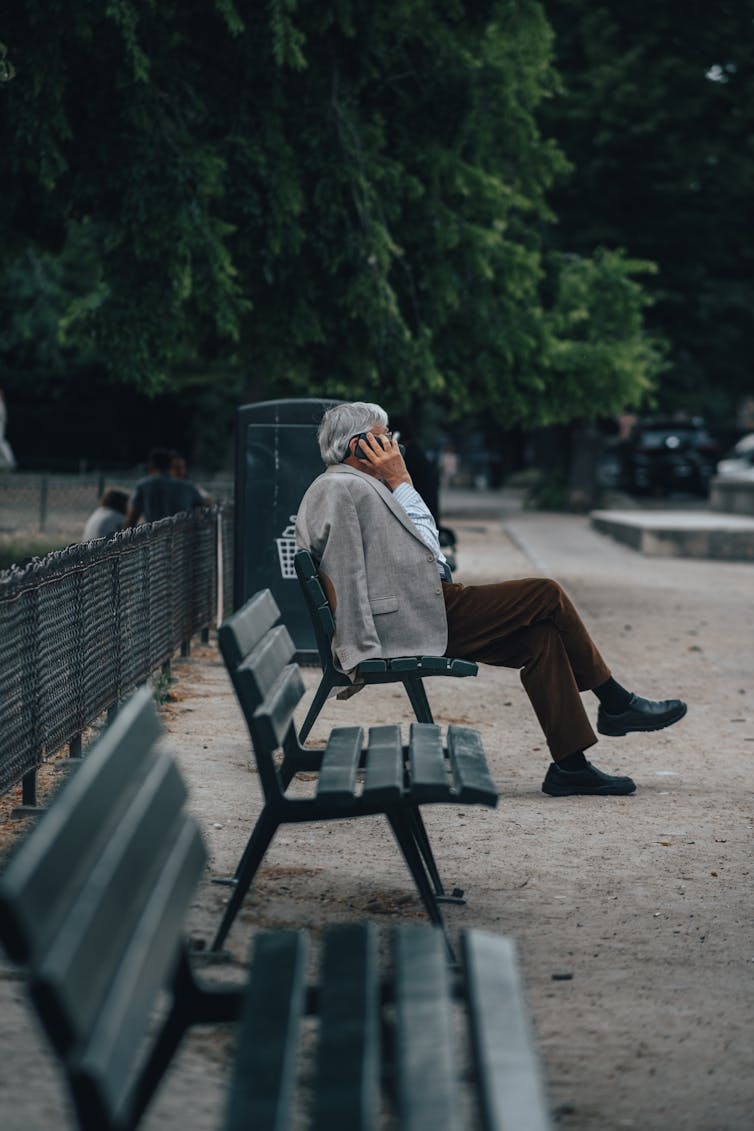 Homme âgé sur un banc de parc, un cellulaire à la main