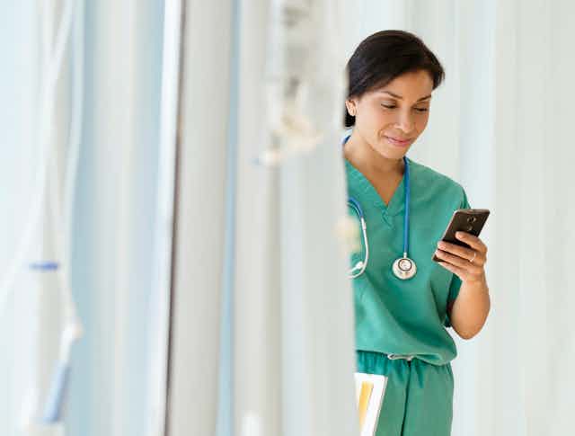 woman in scrubs smiles looking at smartphone