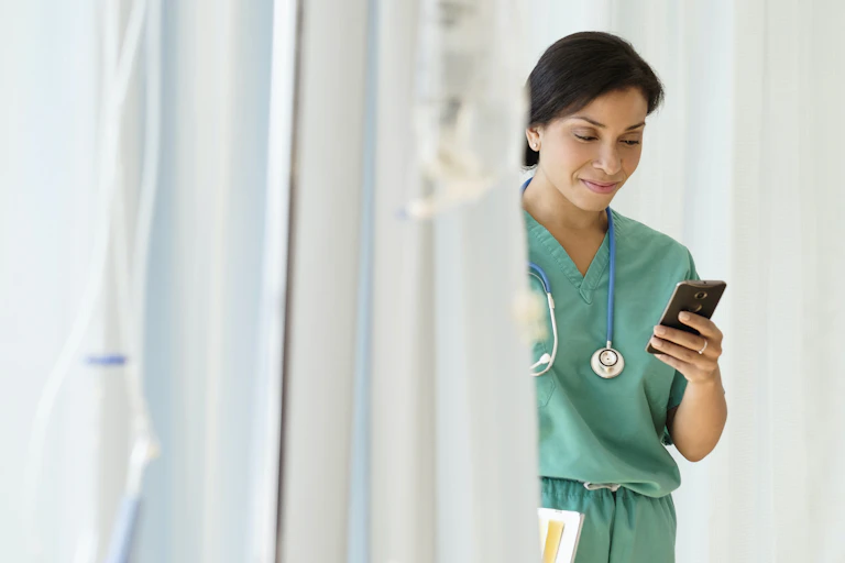 woman in scrubs smiles looking at smartphone