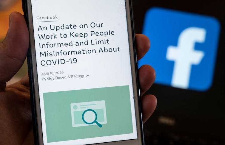 A hand holds a smart phone displaying a message from Facebook about limiting COVID-19 misinformation